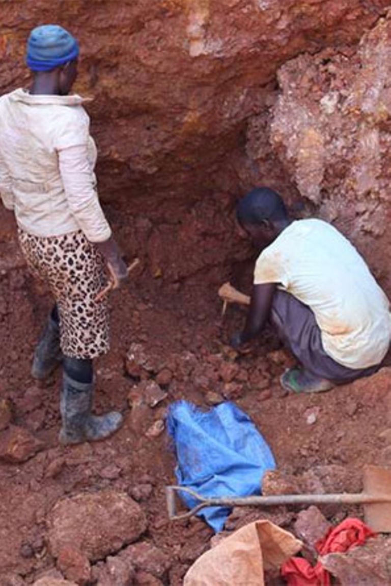 man wearing a black jacket, white shirt, blue jeans, and brown boots, playing a white electric guitar while sitting on an amp